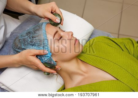 Spa treatment. Facial massage with jade stones. Alternative medicine. Massage of forehead zone. Guasha