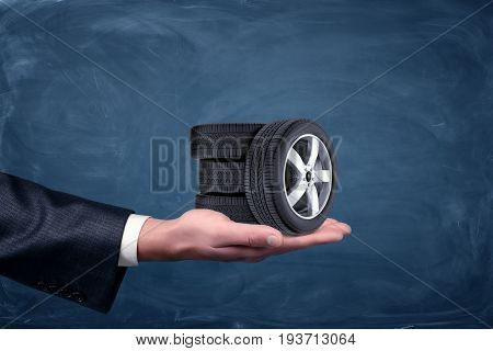 A businessman's hand on blue chalkboard background holding four tiny car wheels. Car service business. Repair shop. Dealership.