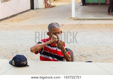 CHIANG RAI THAILAND - MARCH 20 : unidentified old asian leprosy man with cap drinking coffee in paper cup on March 20 2016 in Chiang rai Thailand.