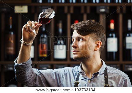 Bokal of red wine on background of male sommelier appreciating color, quality, flavor and sediments of drink. Professional degustation expert in winemaking.