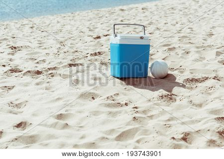 blue cooler box and volleyball ball on sandy beach