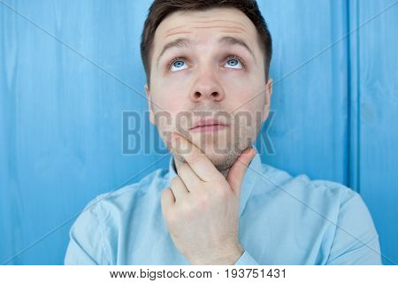 Caucasian thoughtful young man standing by the blue woodenwall. Think about life