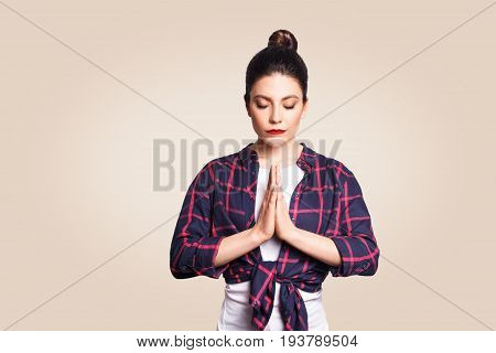Young brunete woman practising yoga holding hands in namaste and keeping her eyes closed. Caucasian girl meditating indoors praying for peace and love having calm and peaceful facial expression.