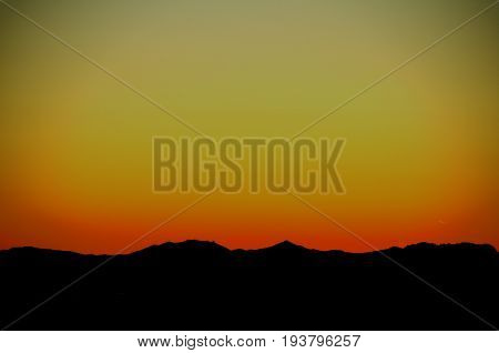 3D illustration of warm colors of the evening sky with a mountain silhouetted against it.