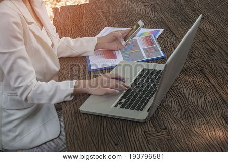 Asian smile beautiful girl sitting outdoor office using smart phone and laptop in nature. Work space with work sheet of business business and lifestyle conceptcopy space