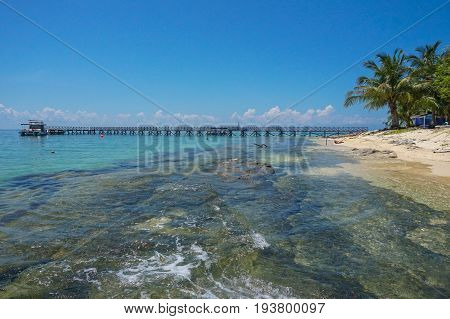 Wooden jetty over the beautiful Rusukan Besar island tropical beach with blue sky and clouds in Labuan Pearl of Borneo,Malaysia.