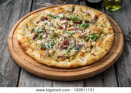 pizza with sun-dried tomatoes, prosciutto, arugula and parmesan cheese on a plate on the table