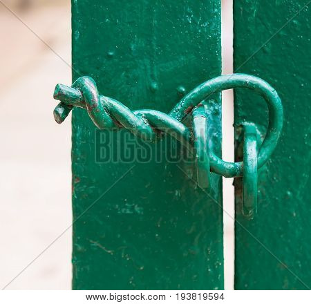 Green fence. The gate is closed. There is no lock. The door is closed with a twisted wire