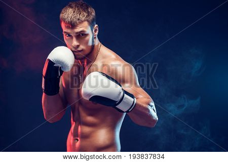Aggressive shirtless boxer on dark smoke background.