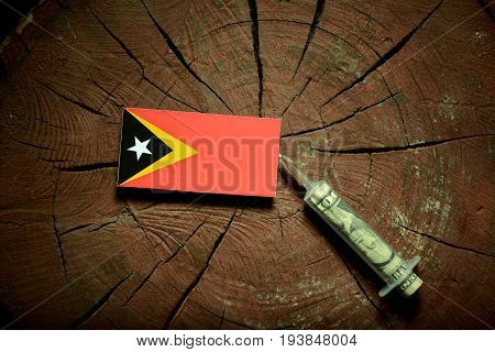 East Timorese Flag On A Stump With Syringe Injecting Money In Flag