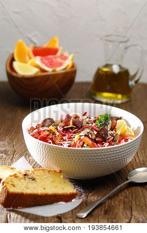 root vegetables salad in a big white bowl on a rustic table, olive oil on the background and a piece of homemade bread
