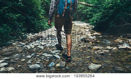 Unrecognizable Traveler Man With Backpack Walks Along Mouth Of Mountain River In Forest Rear View. Trek Hiking Destination Experience Lifestyle Concept