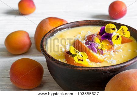 bowl of homemade yellow smoothie with fresh mango peaches and apricots topped with coconut and flowers over rustic wooden background. close up. healthy breakfast