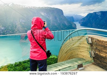 Tourism and travel. Woman tourist nature photographer taking photo with camera enjoying Aurland fjord landscape from Stegastein lookout Norway Scandinavia.