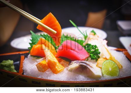 Salmon slice sashimi in chopsticks . Fresh made Sushi set with salmon octopus scomberand wasabi. Traditional Japanese cuisine.