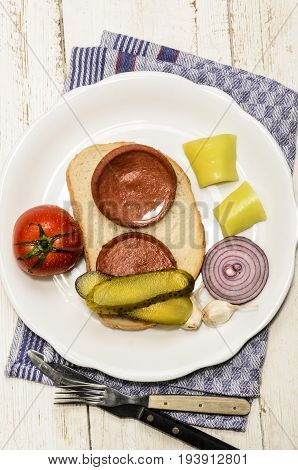 grilled scalded sausage a slice of bread with fresh tomato gherkin yellow paprika onion and garlic on a plate