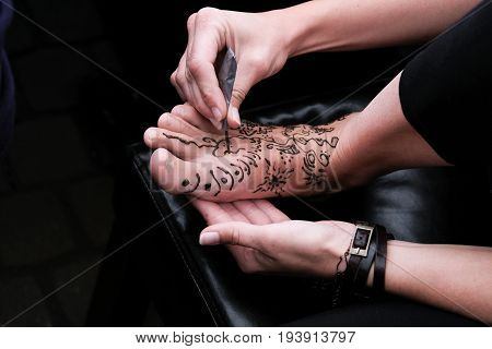 Woman applying henna on female foot. close up