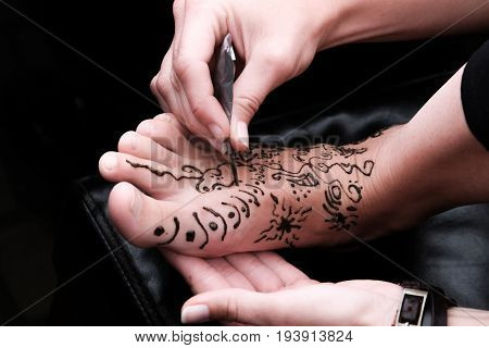 Woman applying henna on female foot. close up