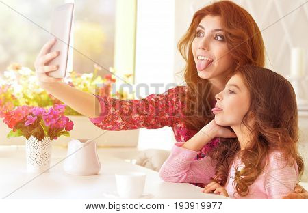 Beautiful  young woman and little girl  sitting at  table and using  tablet taking selfie