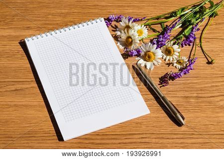 Mocap. Notepad with white paper and pen ,decorated with a bouquet of wild flowers on a wooden table
