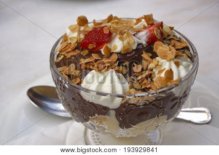 Chocolate profiterole pastry closeup served on a glass bowl with spoon.
Puff pastry with dark chocolate choux covered with whipped cream, garnished with almonds and strawberry.
