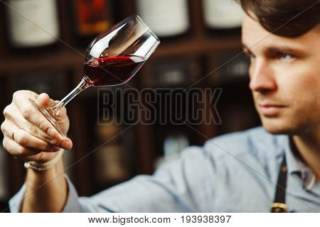 Bokal of red wine on background of male sommelier appreciating color, quality, flavor and sediments of drink. Professional degustation expert in winemaking.