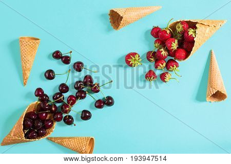 Berries in waffle cones - strawberry and black cherry on blue background. Top view. Copy space. Still life mockup flat lay