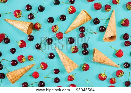 Berries in waffle cones - strawberry and black cherry on blue background. Top view. Copy space. Still life mockup flat lay