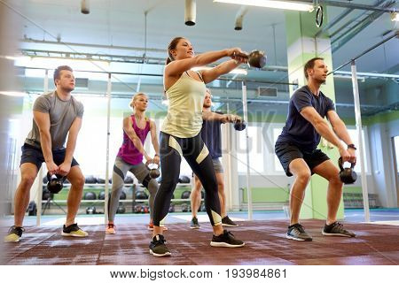 sport, fitness, weightlifting and training concept - group of people with kettlebells exercising in gym