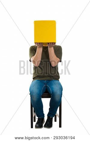 Full Length Portrait Of Casual Incognito Young Man Seated On A Chair Holding A Yellow Box Instead Of
