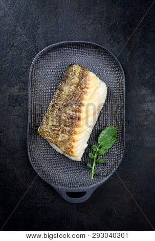 Fried Japanese skrei cod fish filet with wasabi lettuce as top view on a modern design plate 