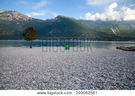 Young man sitting in front of mountain and lake landscape at Garda Lake, Italy. - Travel, summer vacacion concept.