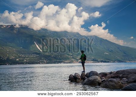 Young man standing in front of mountain and lake landscape at Garda Lake, Italy. - Travel, summer vacacion concept.