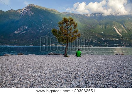Young man sitting in front of mountain and lake landscape at Garda Lake, Italy. - Travel, summer vacacion concept.