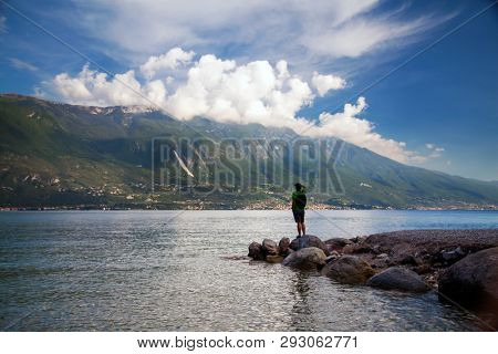 Young man standing in front of mountain and lake landscape at Garda Lake, Italy. - Travel, summer vacacion concept.
