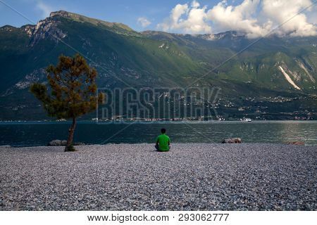 Young man sitting in front of mountain and lake landscape at Garda Lake, Italy. - Travel, summer vacacion concept.