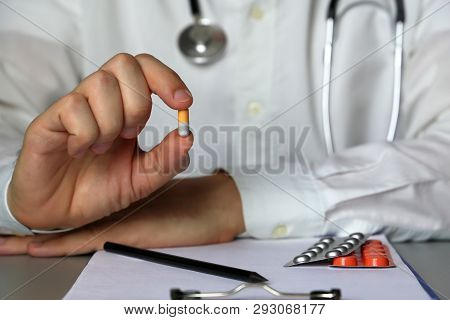 Physician Sitting In Hospital Office With Pill In Hand, Doctor At Work Giving Medication In Capsules