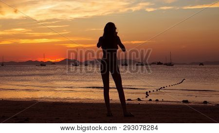 Girl Holding Smart Phone And Taking Red Sunset Photo On The Tropical Beach.  Silhouette Of A Woman, 