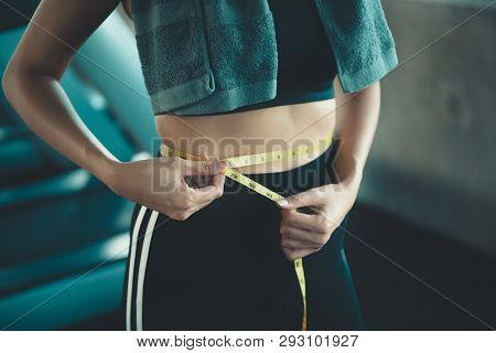 Portrait Of Beautiful Woman Showing Successful Weight Loss With Measuring Tap In Fitness Gym Backgro