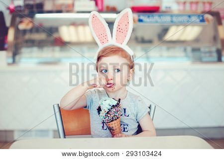 Cute Funny Caucasian Blonde Girl Child With Blue Eyes Wearing Headband With Easter Bunny Ears Eating