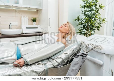 Blonde Girl Lying With Closed Eyes During Pressotherapy Session In Clinic