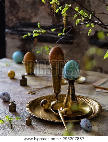 Easter Eggs Painted With Natural Dyes Standing On Brass Golden Stacks And Plate On Concrete Backgrou