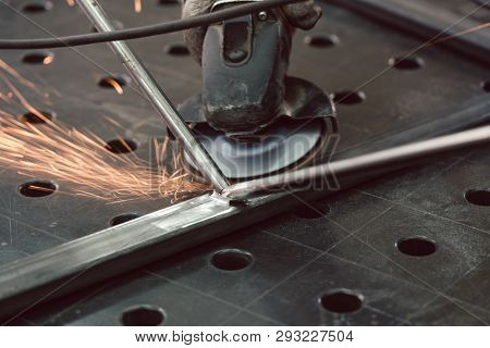 Worker in metal factory grinding workpiece with disk grinder, sparks flying