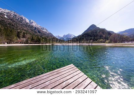 Wooden Dock On Lake Jasna With Mountains Razor And Prisojnik On The Horizont In Slovenia