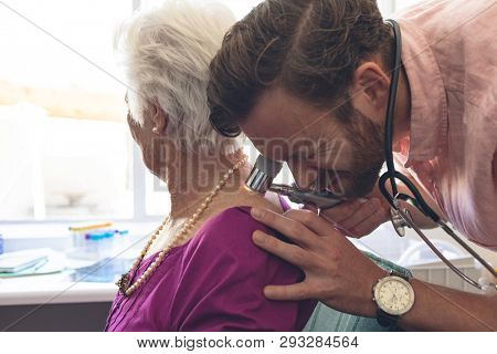 Side view of Caucasian Male dermatologist examining senior patient through dermatoscopy