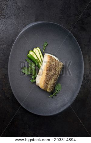 Fried Danish skrei cod fish filet with baby zucchini and lettuce as top view on a modern design plate 