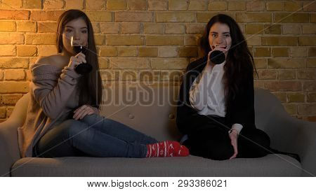 Closeup Portrait Of Two Young Pretty Women Watching Tv And Chilling With Wine While Resting In A Coz