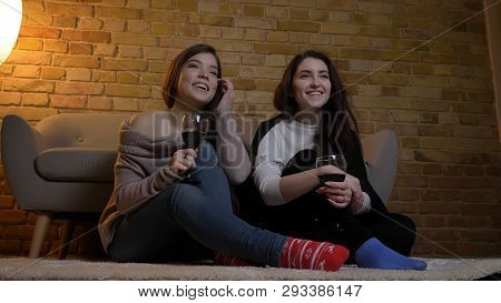 Closeup Portrait Of Two Young Pretty Women Watching Tv And Chilling With Wine While Sitting On The F