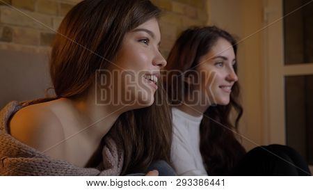 Closeup Portrait Of Two Young Pretty Women Watching Tv With Excitement And Surprise In A Cozy Apartm