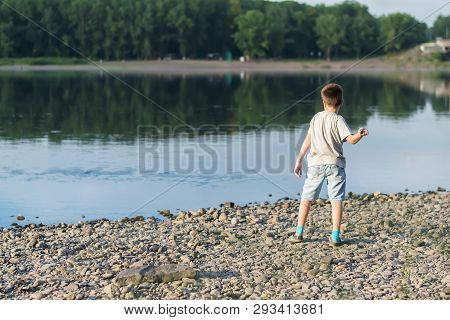 A Child, A Teenager, On A Stony Shore Throws Stones Into The River, Lake